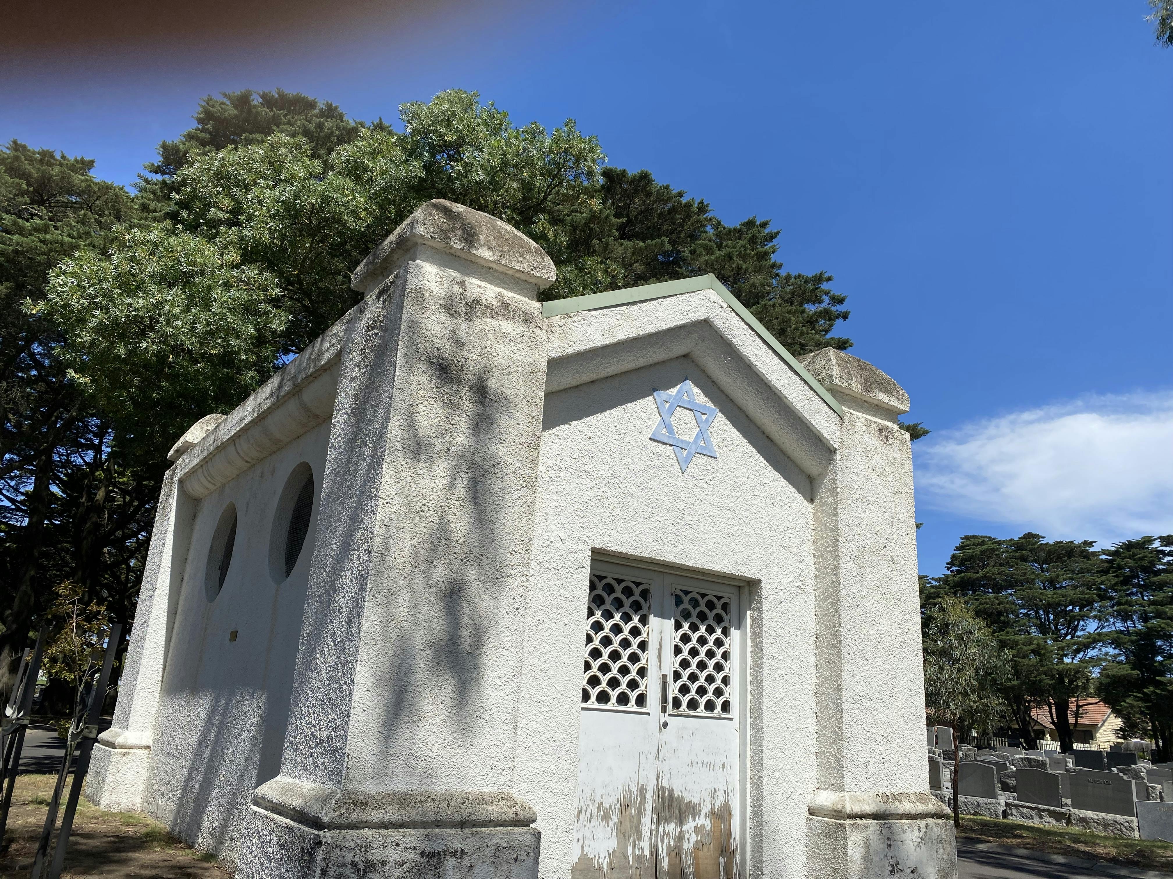 Image of Jewish mortuary chapel dominated by massive corner piers with domed tops and a surface of white painted rough cast render.