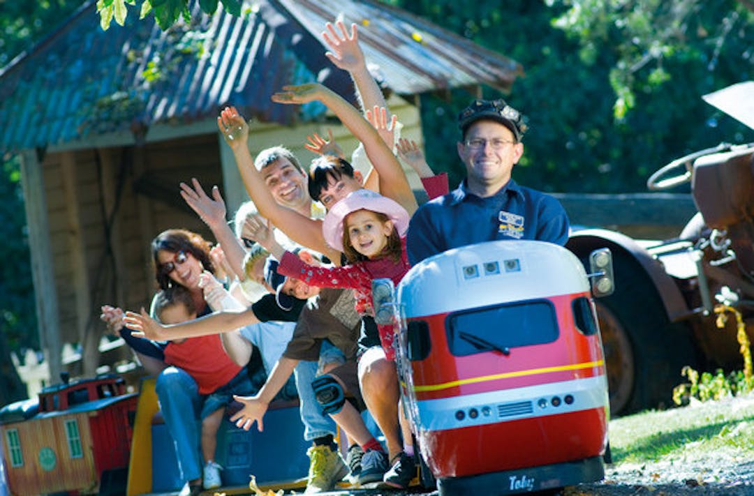 People smiling and waving while they ride the miniature railway train.