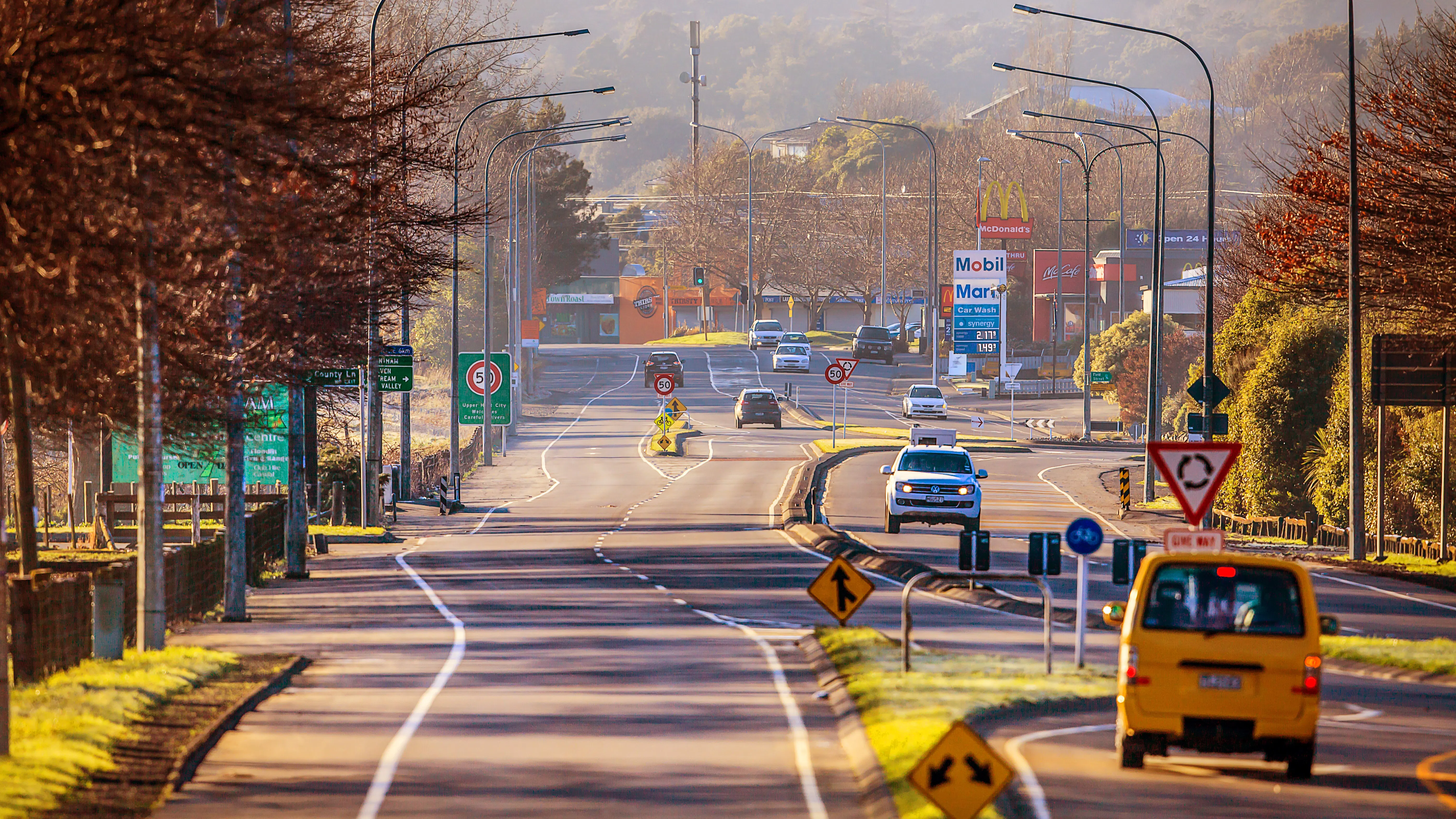 Long stretch of road with trees lining the left side of the road and vehicles on the right side of the road