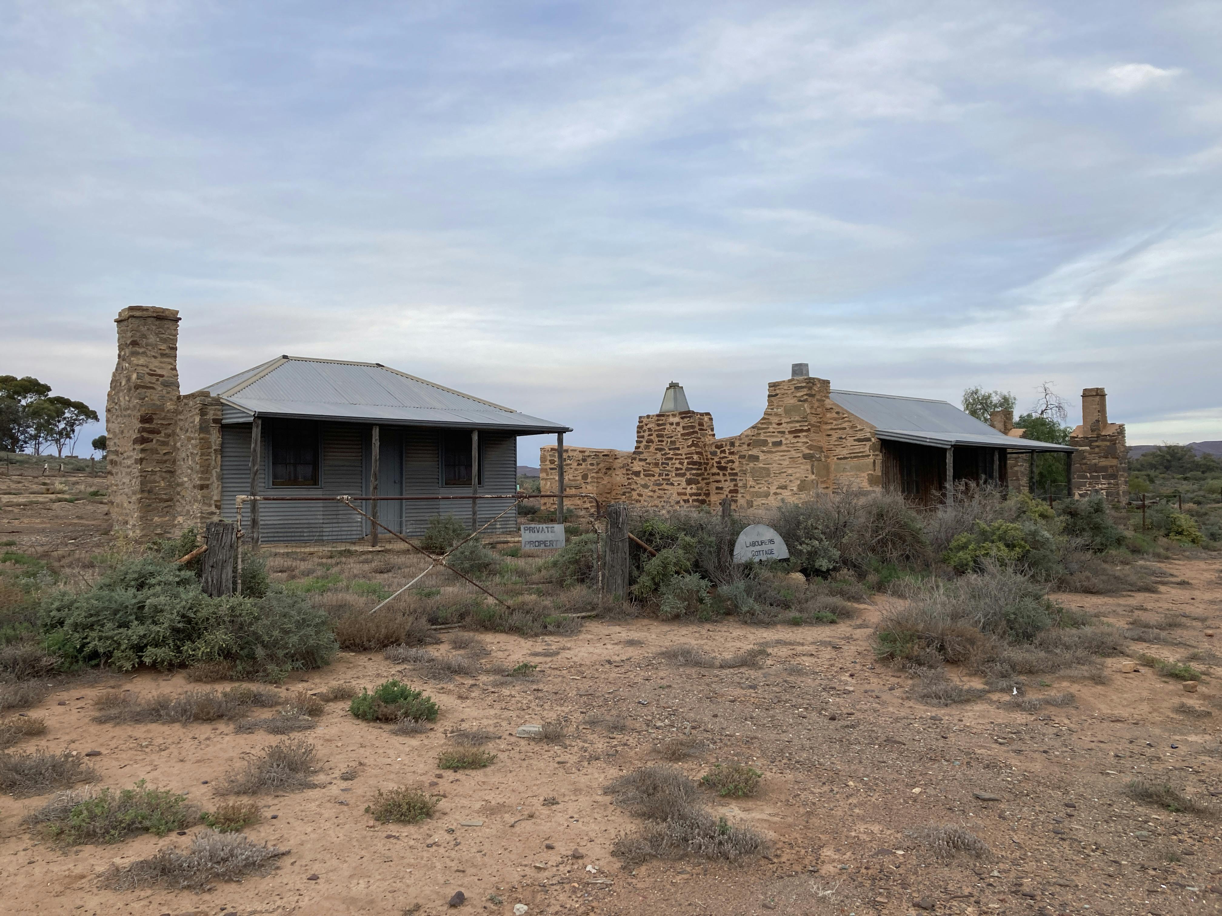 Small buildings made of stone and corrugated iron in an arid outback landscape
