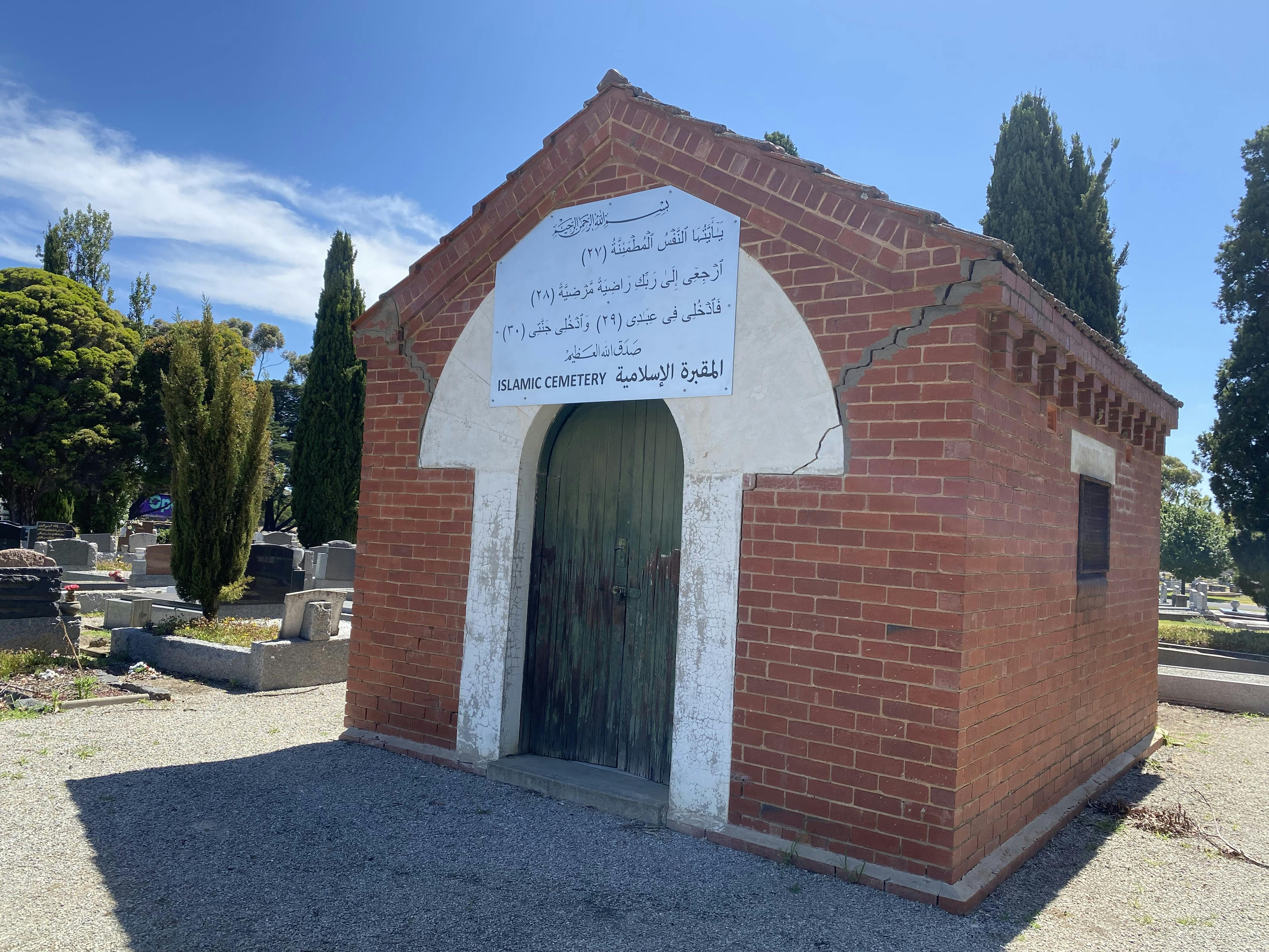 A red brick Islamic chapel with graves in the background.