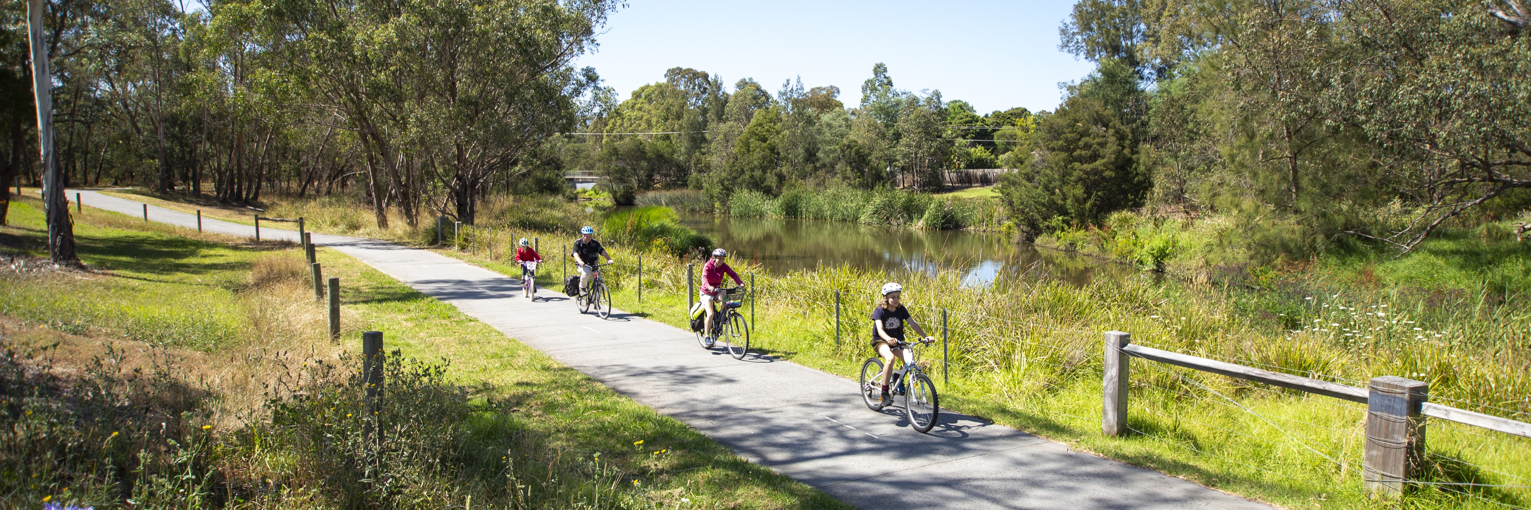 A family riding their bicycles along a path next to a creek.