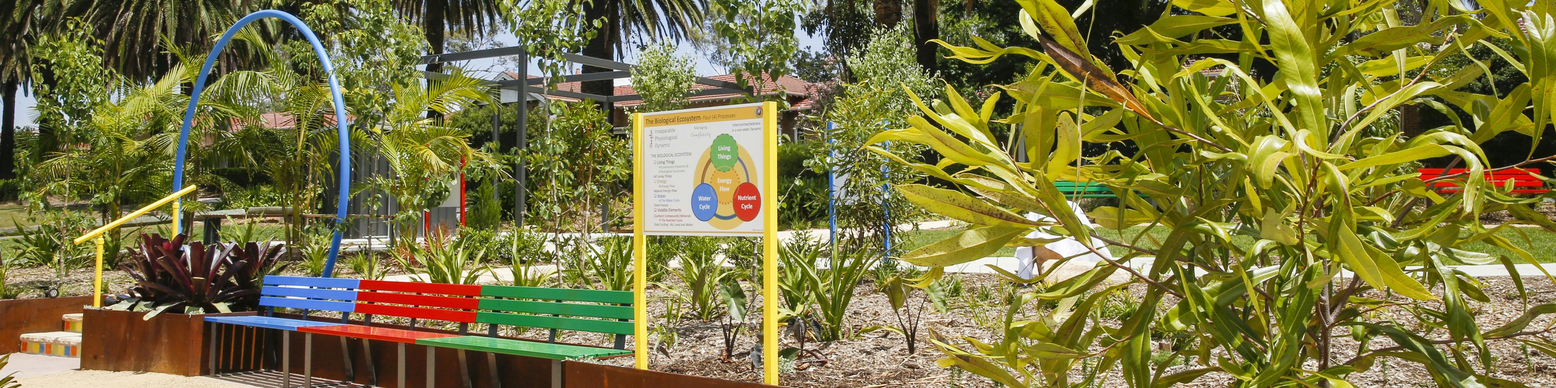 Balcombe heights estate sensory garden with blue, red, green benches and a informational sign at the foreground.