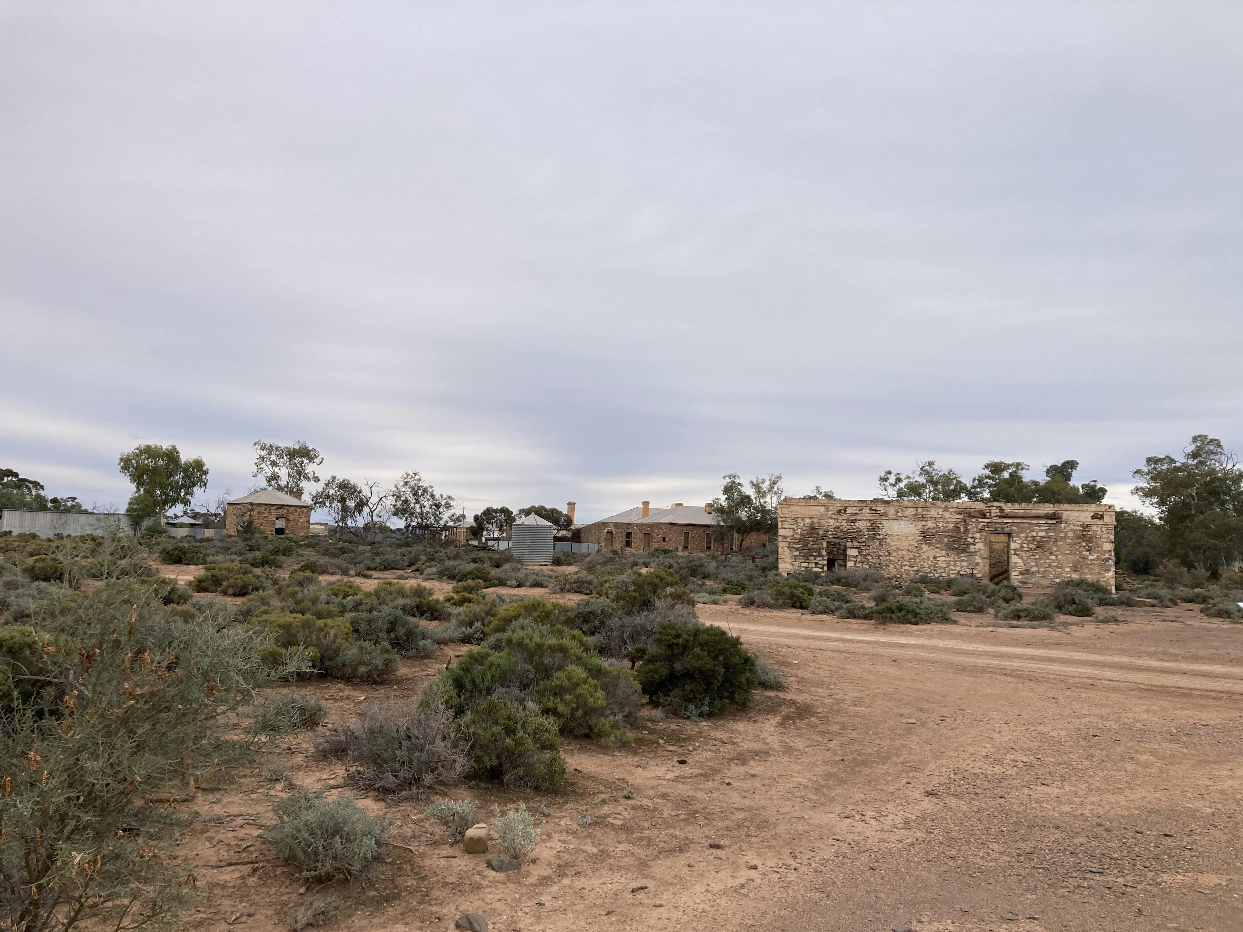 A dirt road, some small intact stone buildings and a ruin with no roof, but stone walls still standing.