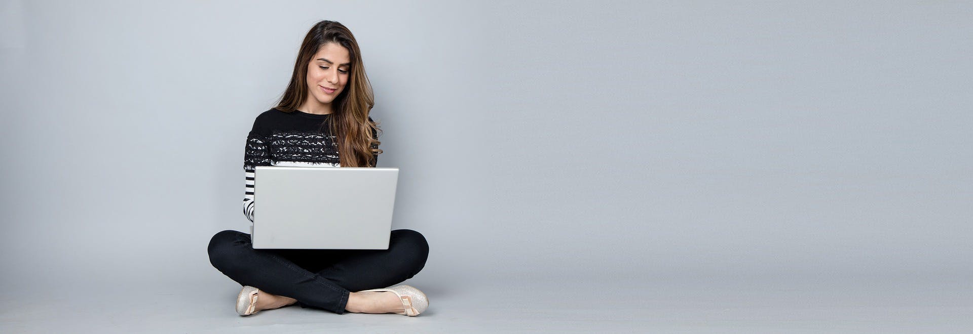 A woman sitting crosses legged with a laptop in her lap. 