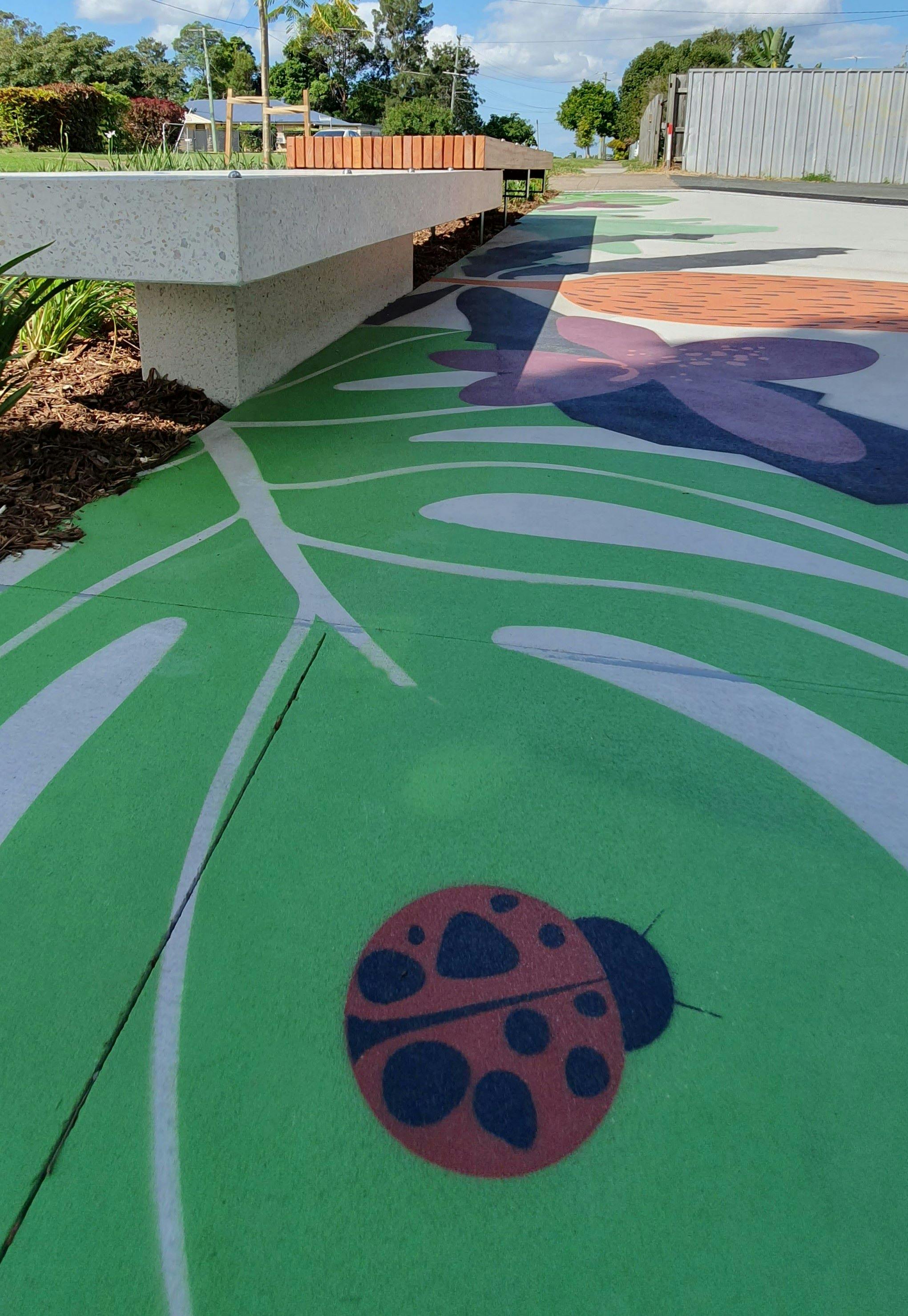 Lumley St eastern entrance looking at new seating area with street tree and planting bed and 'Echidna Magic' pavement design detail of lady bug and native flowers and leaves.