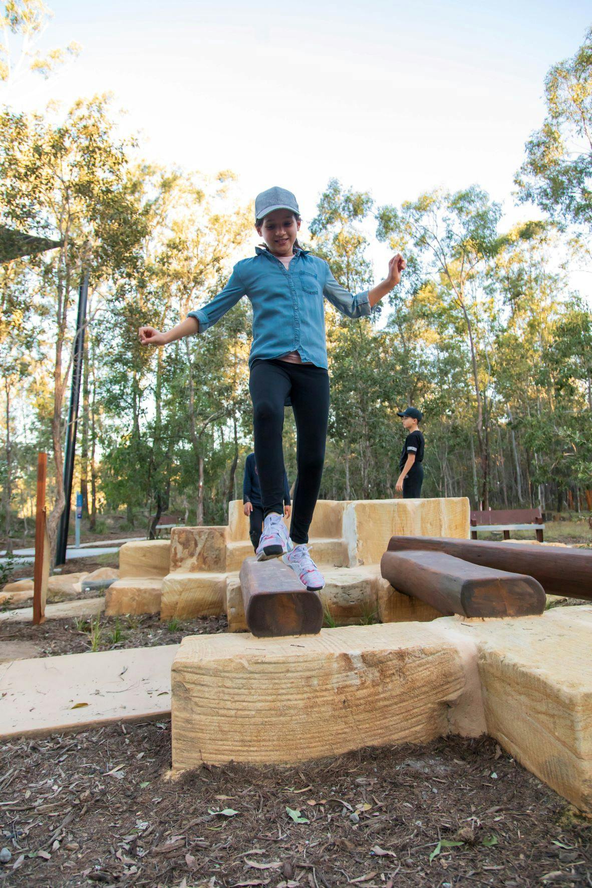 Young person navigating balance on tree trunk and sandstone blocks. 