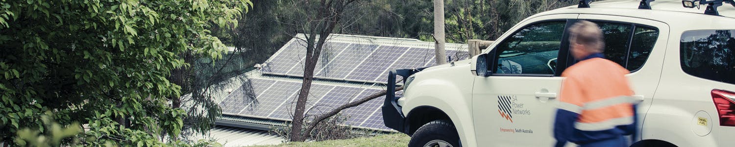 Solar panels on roof of house in background with vehicle and person in foreground.