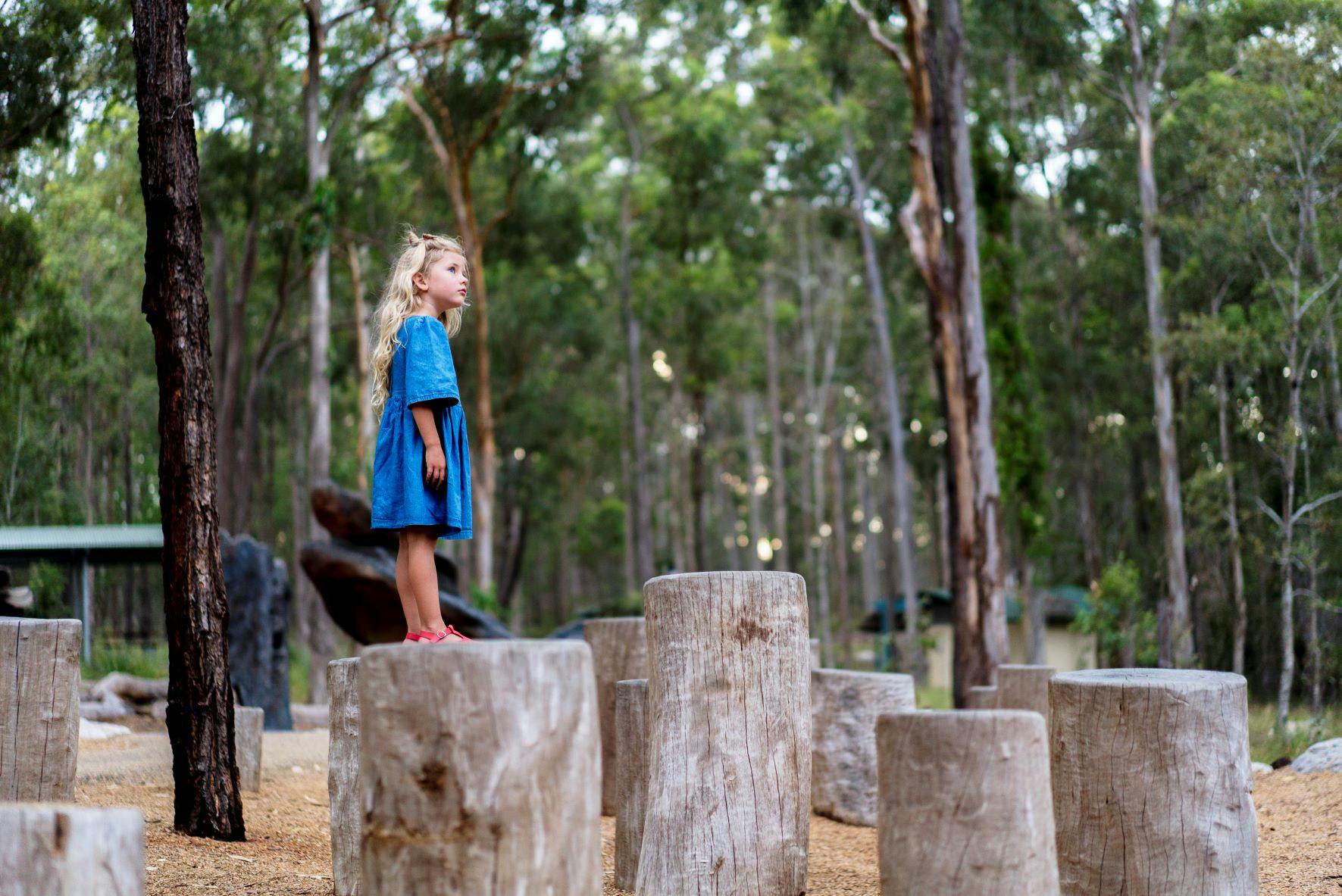 Girl balancing and jumping across the tree stumps.