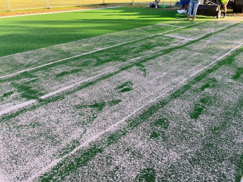 Fine sand being spread along the length of the synthetic surface