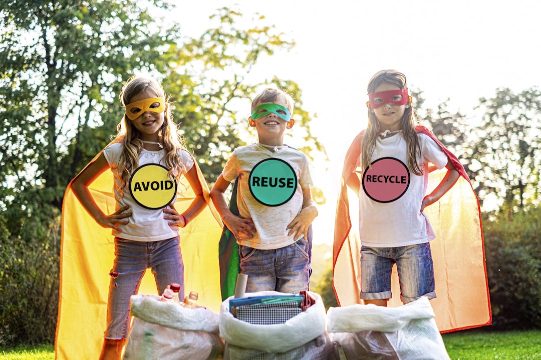 Three children dressed as superheroes with 'Avoid' 'Reuse' and 'Recycle' messaging
