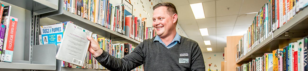 A librarian getting a book from a shelf surrounded by other books and resources