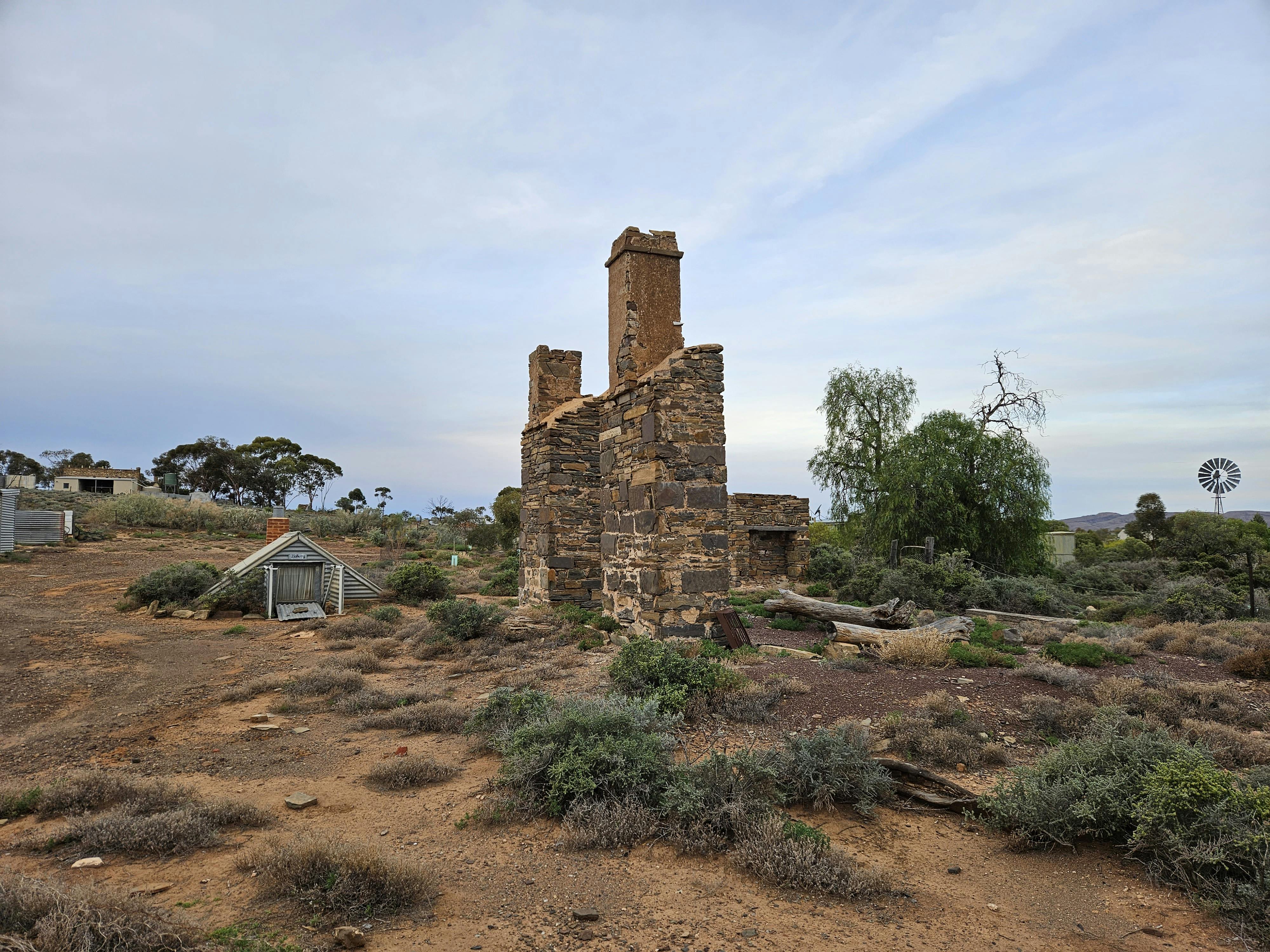 Two remnant stone chimneys and a small triangular structure like a roof, with a small entrance, sitting on the ground.