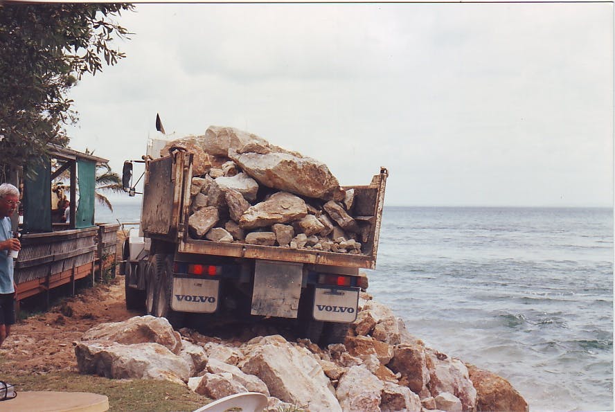 Early slide barriers - Semi-trailers dumping rocks to create a rock wall at Amity Pt