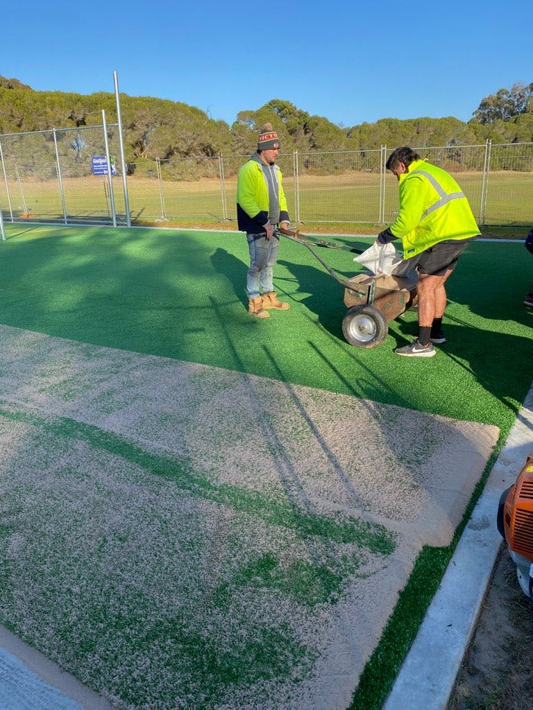 Fine sand being spread over the synthetic grass surface