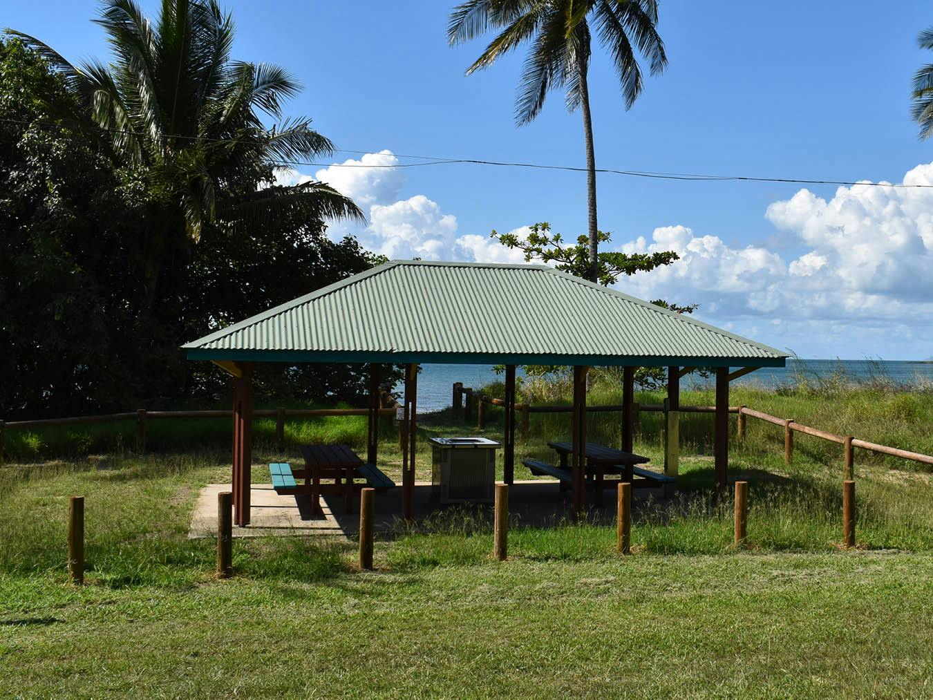 This view is from directly opposite a shelter on the asphalt track. The shelter includes a double BBQ facilitiy and shades two older-style timber picnic settings. Beach access is located directly behind the shelter.