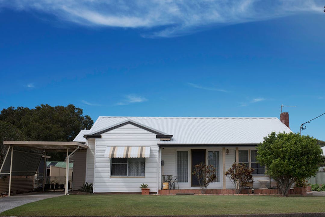 Image of a weatherboard white house with a bright blue sky above