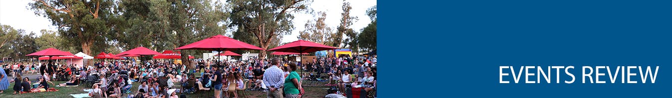 A crowd of people enjoying a picnic in a park under big red umbrellas