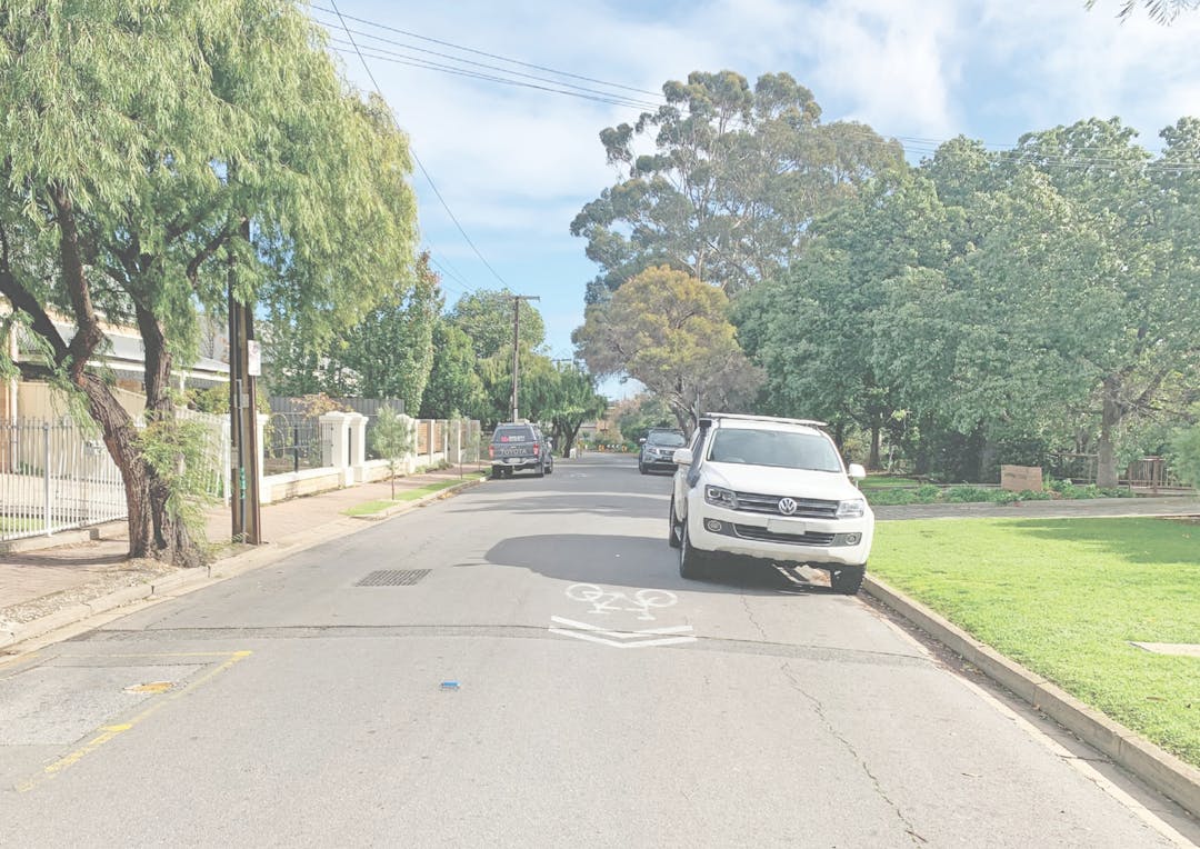 Photo of shared path adjacent King William Road showing two bike riders on the road and one on the path, plus cars passing.