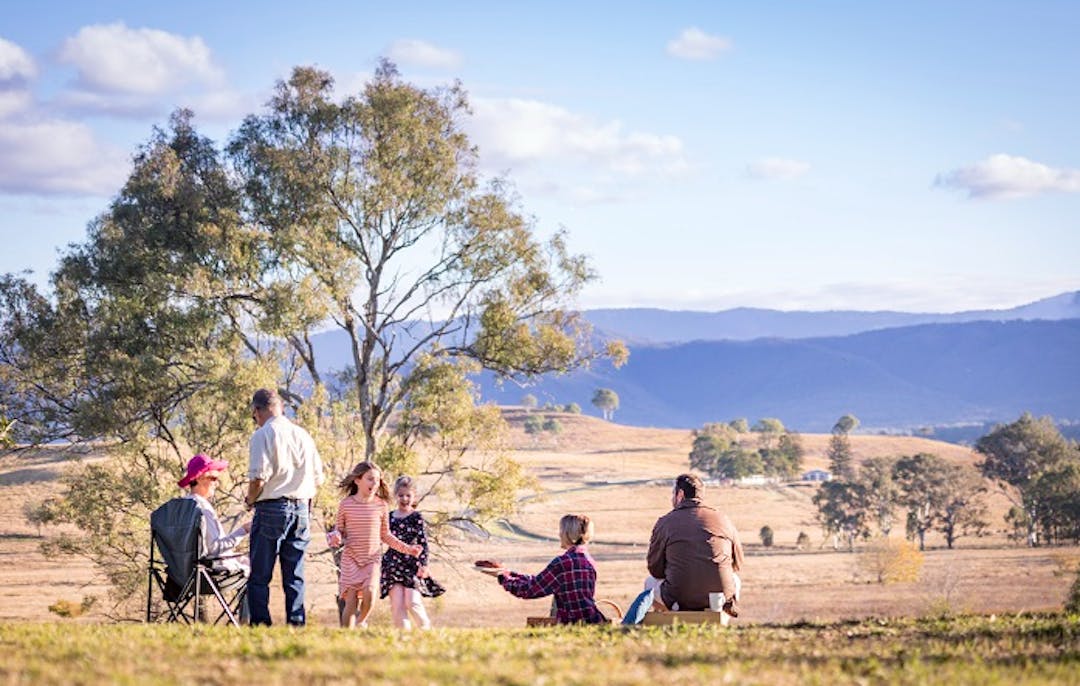 Family picnic sitting with their backs to the camera, looking at open grassland and mountains in the distance