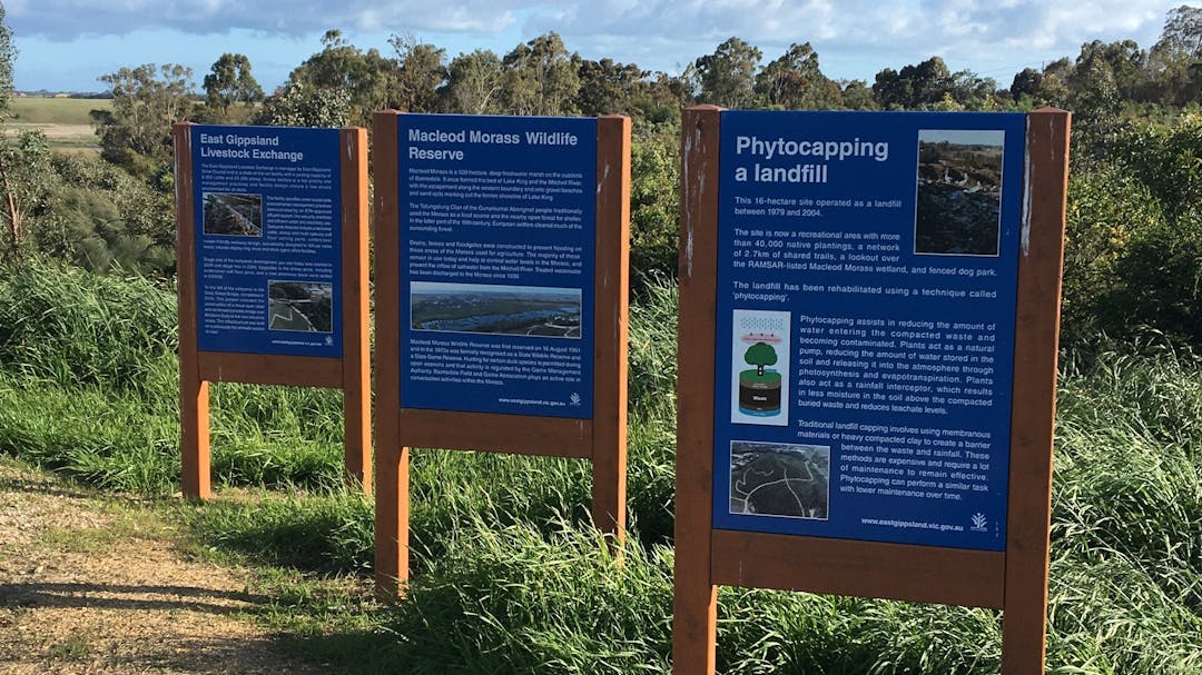 Three large information signs along a gravel path in bushland.