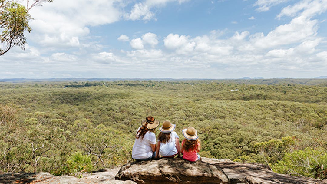 Woman and her daughters sitting on a rock looking over the Blue Mountains National Park