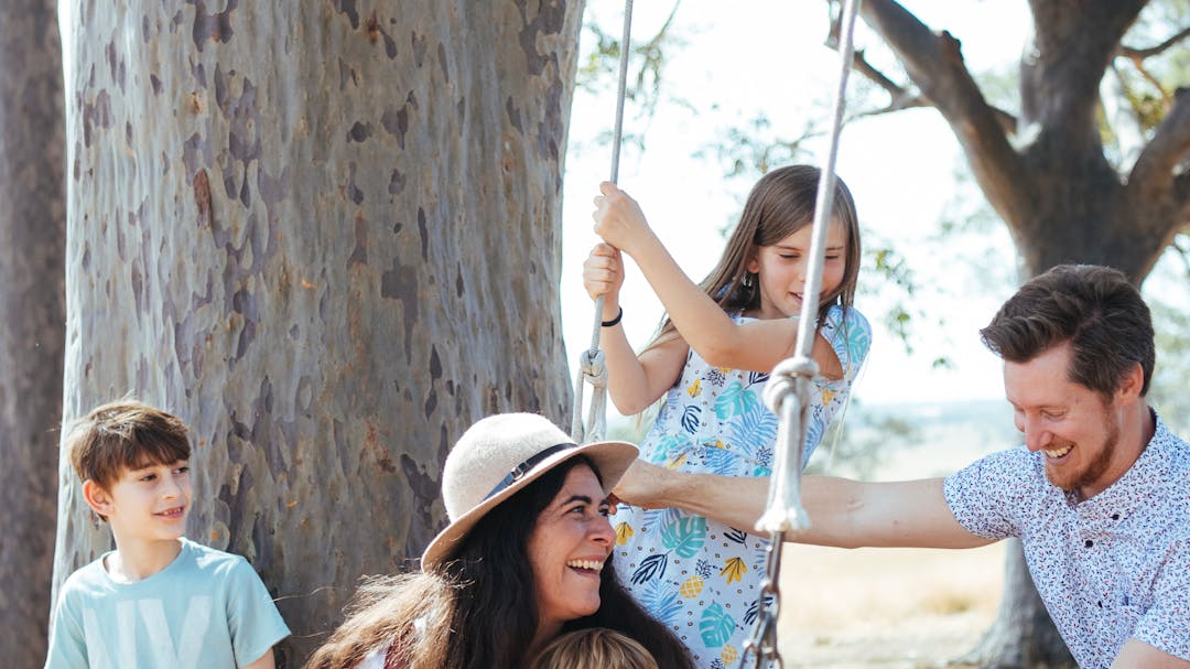 Family playing on a rope swing in a forest.