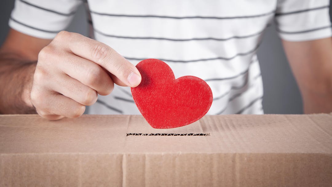 person placing red heart in donations box