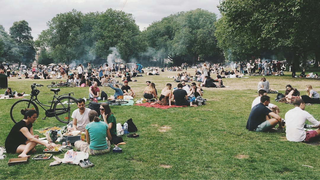 people gathering together in an open grassy space, with bikes and food and picnic baskets