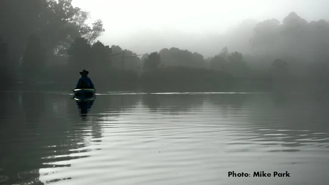 Photo of a man paddling a canoe on a lake.