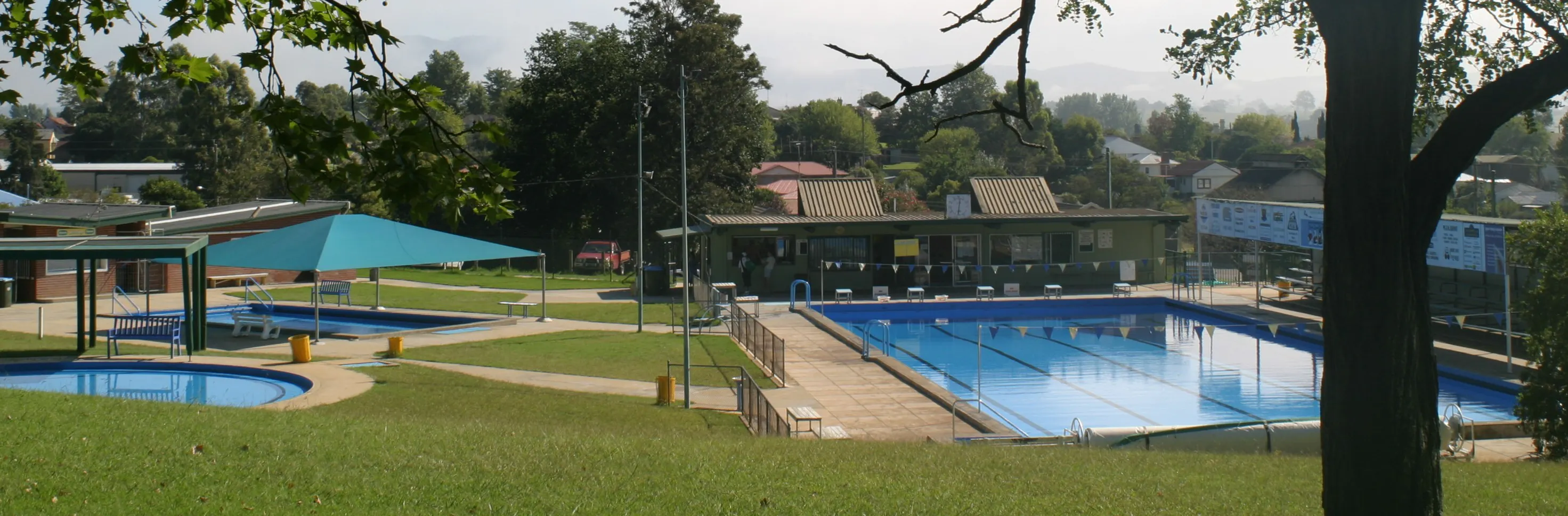Three swimming pools, small round, medium with green shade cover, large lap pool.