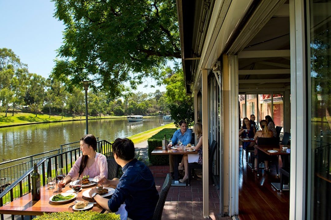 People dining in the Jolleys Boathouse Bistro with a view of the River Torrens in the background.   