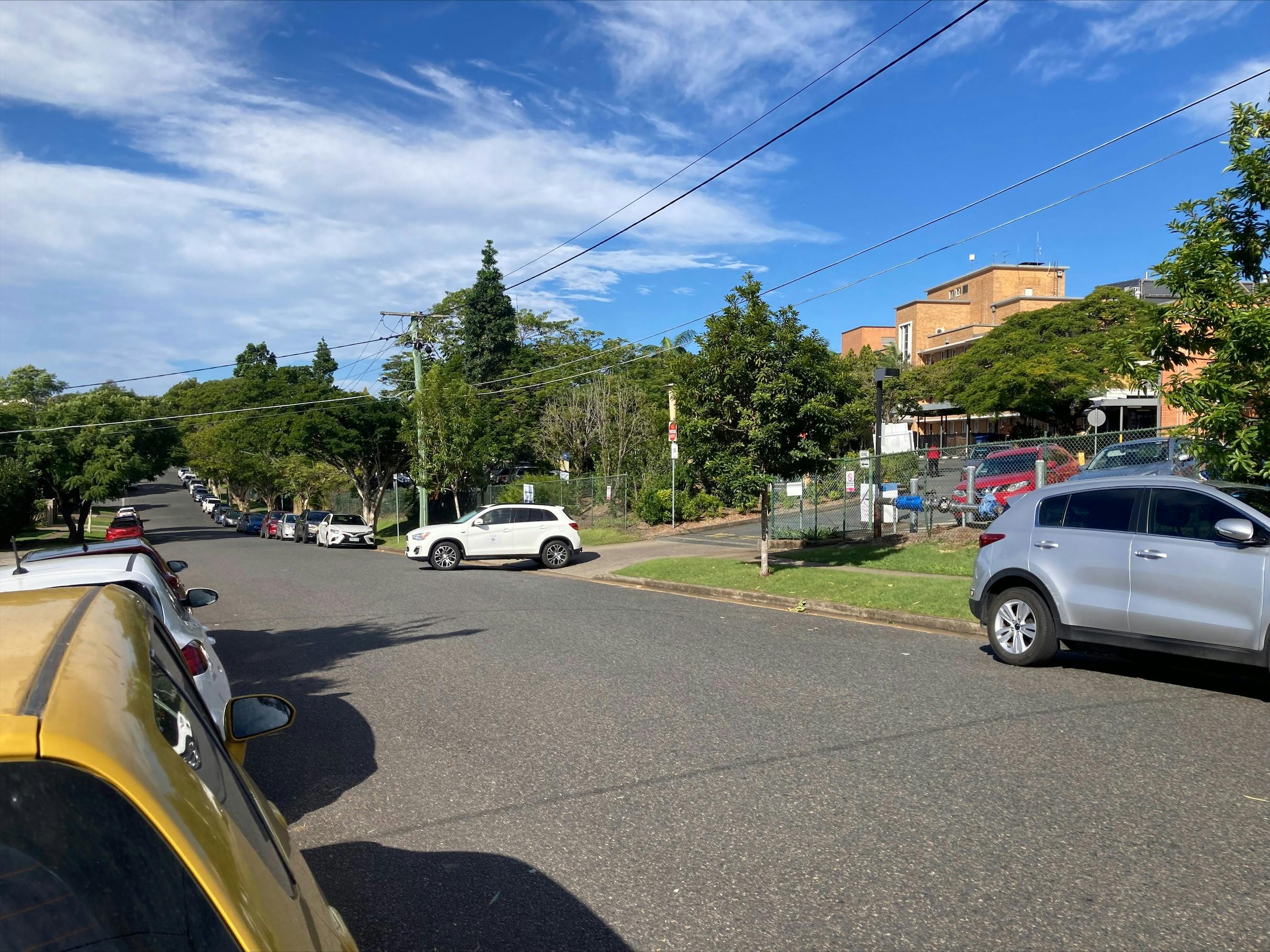 Photo of cars parked along Denman Street, Greenslopes beside the exit to one of the Greenslopes Private Hospital carparks.