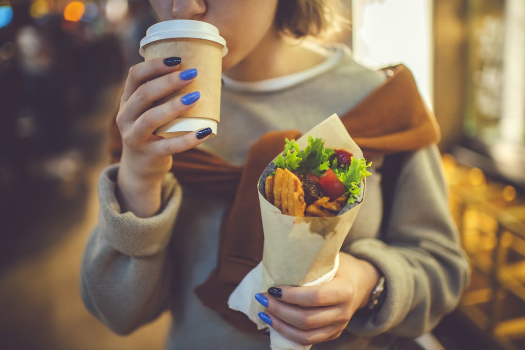 Young person sipping from a compostable cup and holding street food in their other hand.