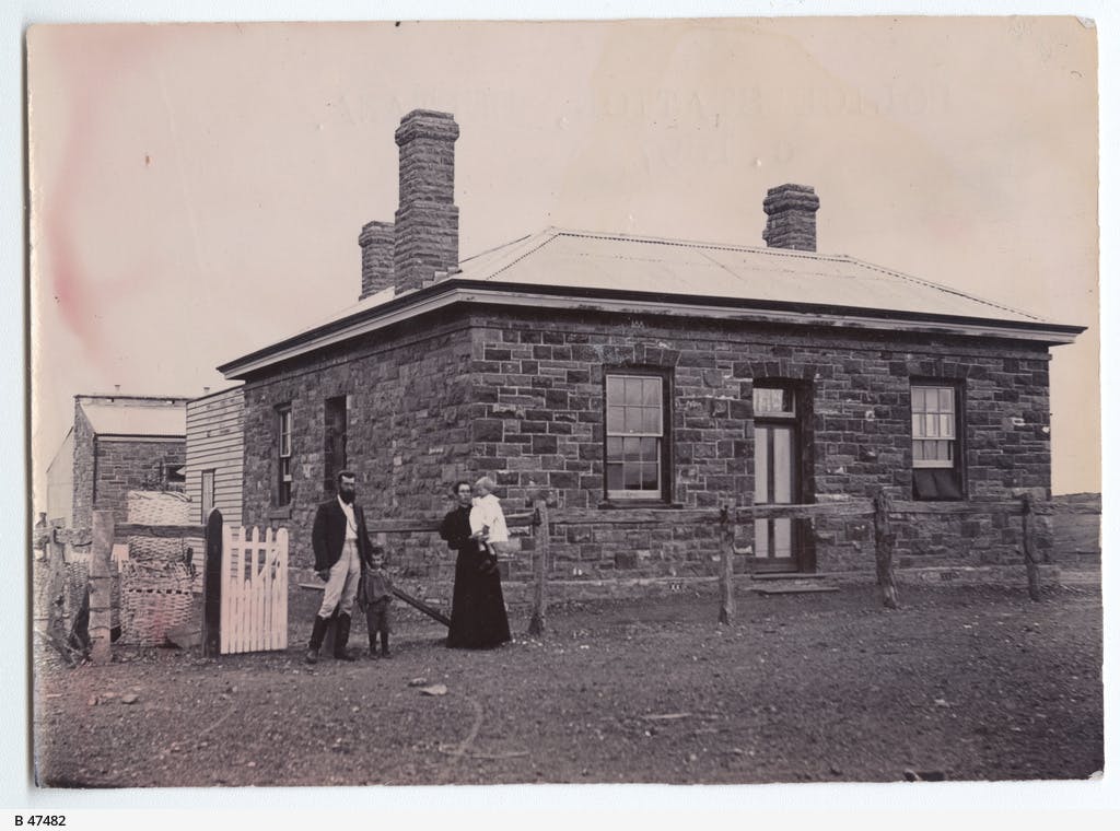 Black and white photo shows a family standing outside the Beltana Police Station in 1897. It is a sturdy, square, single storey stone building with three chimneys.