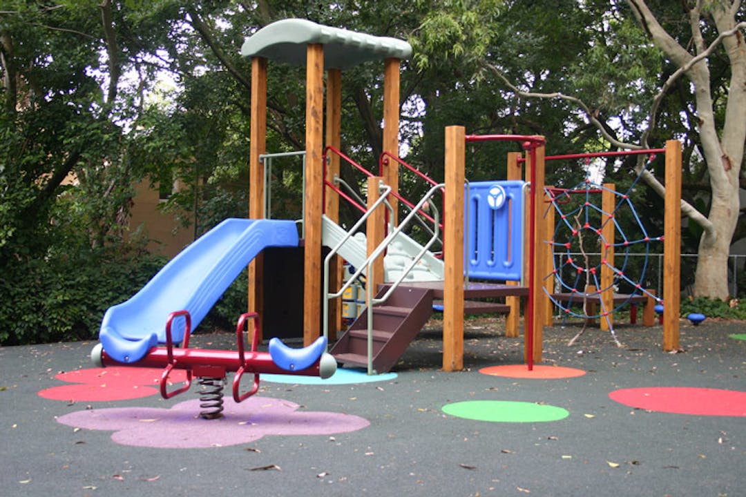 Playground at Dillon St Reserve Image of the existing play equipment at Dillon Street Reserve, Paddington. It includes a slide off a raised decks with steps and a spring toy in the foreground. In the background there are trees and vegetation.