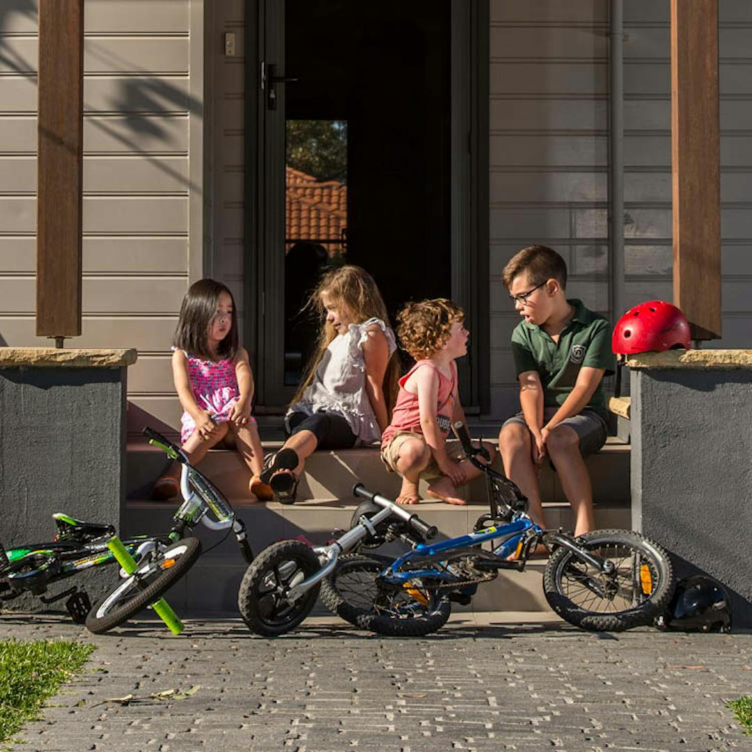 four children talking on front veranda, three bicyles at the front.