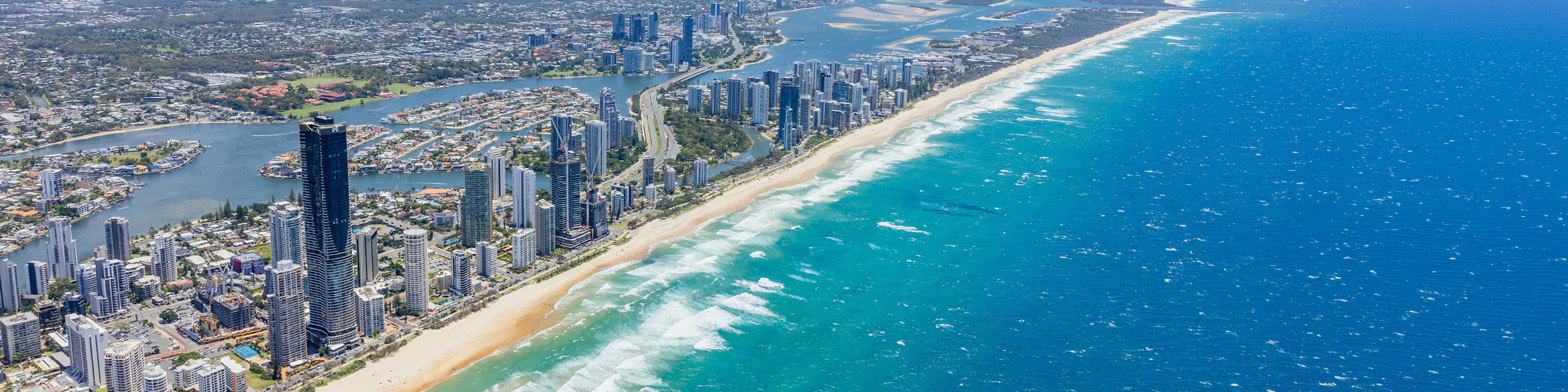 Aerial view of the northern Gold Coast coastline showing high‑rise buildings, sandy beach, ocean waves, and inland waterways