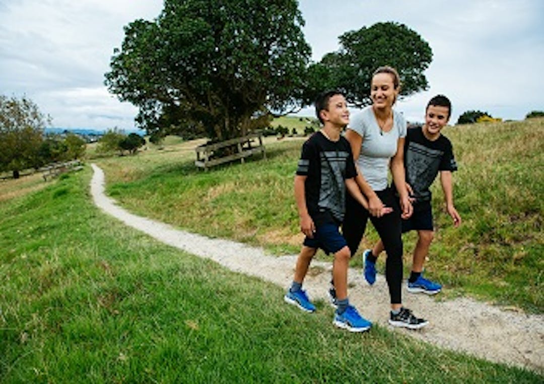 Mother and two sons stroll through Totara Park A mother and two sons stroll along a white stoned walk path running through Totara Park. Surrounding the path is green grass with some trees in the background.