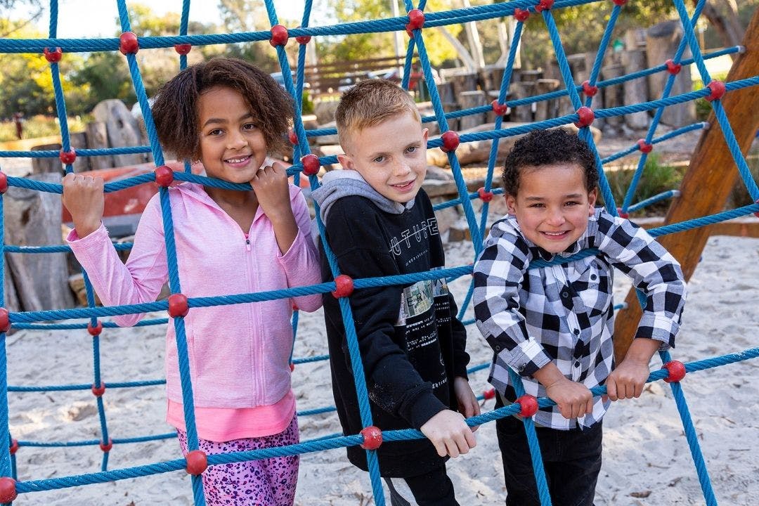 Children playing at local playground, smiling as they climb on climbing net.