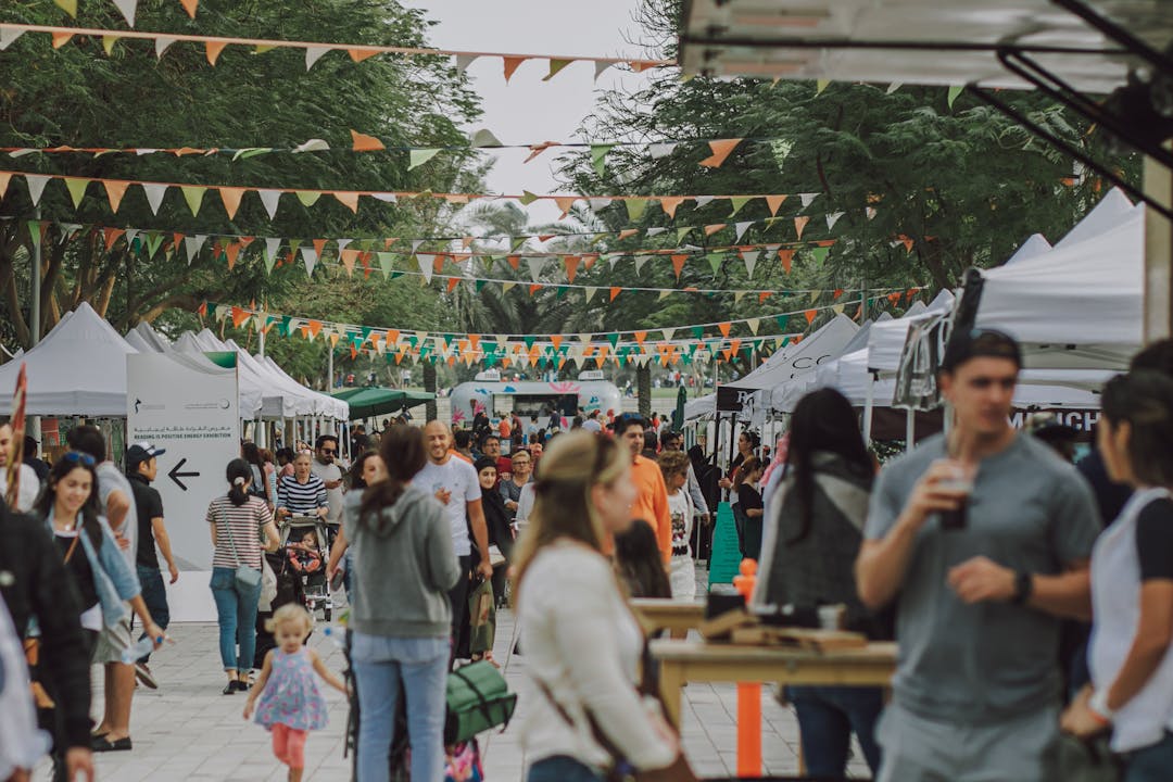 A community festival. People drinking and talking at bar tables. There is bunting hung over the courtyard.