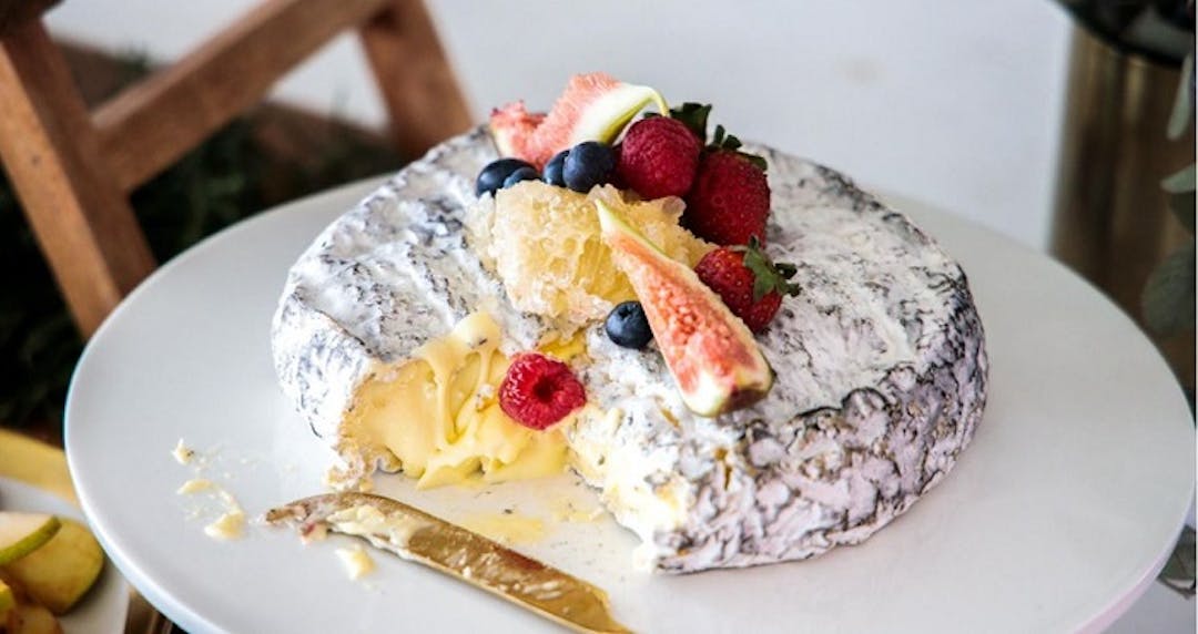 A round of cheese topped with fresh figs, orange and berries