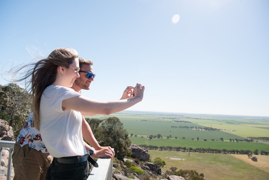 Two people on the lookout at Mount Arapiles with green farm land in the background