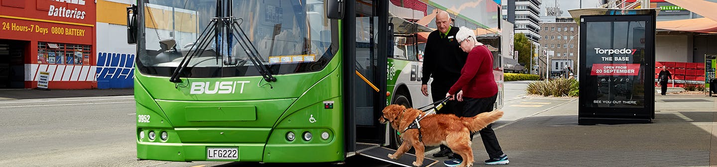 Lady with white hair being helped on the bus with a service dog and man by her side