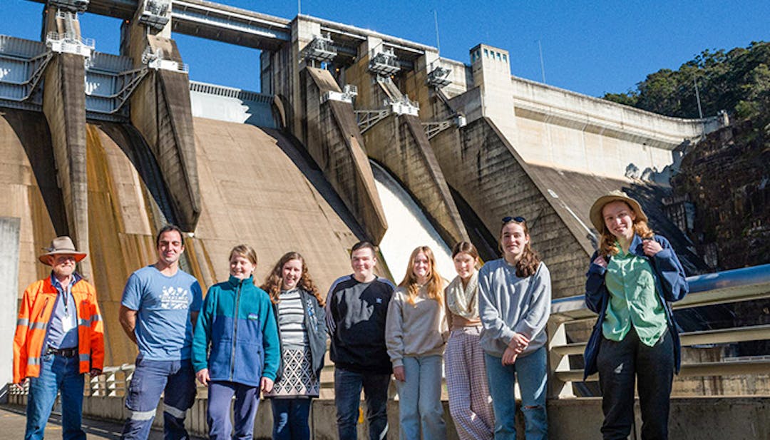 Male and female teenagers standing in a line, in front of a dam