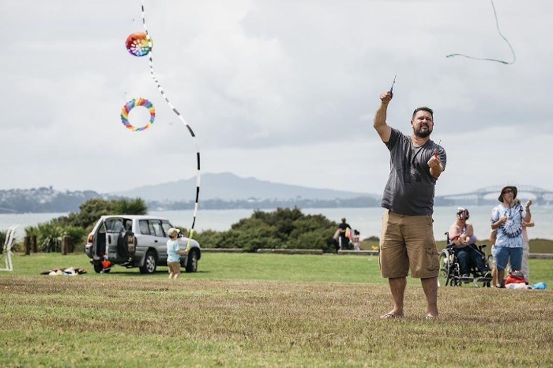Kite flying Man in foreground flying a kite with people in background and Rangitoto in the distance